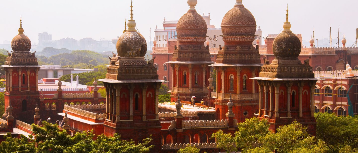 Historic red sandstone domes and minarets of the Madras High Court building surrounded by greenery in Chennai, India.