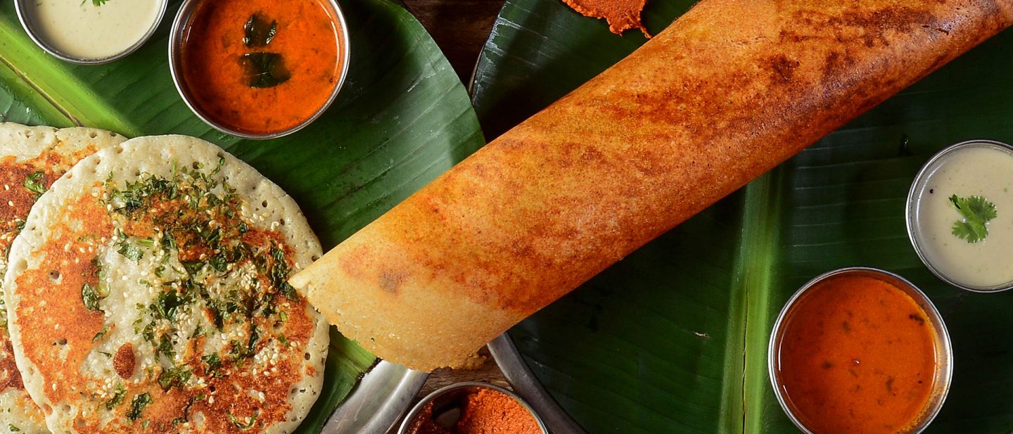 South Indian dosa and uttapam served on banana leaves with coconut chutney, sambar, and spicy red chutney.