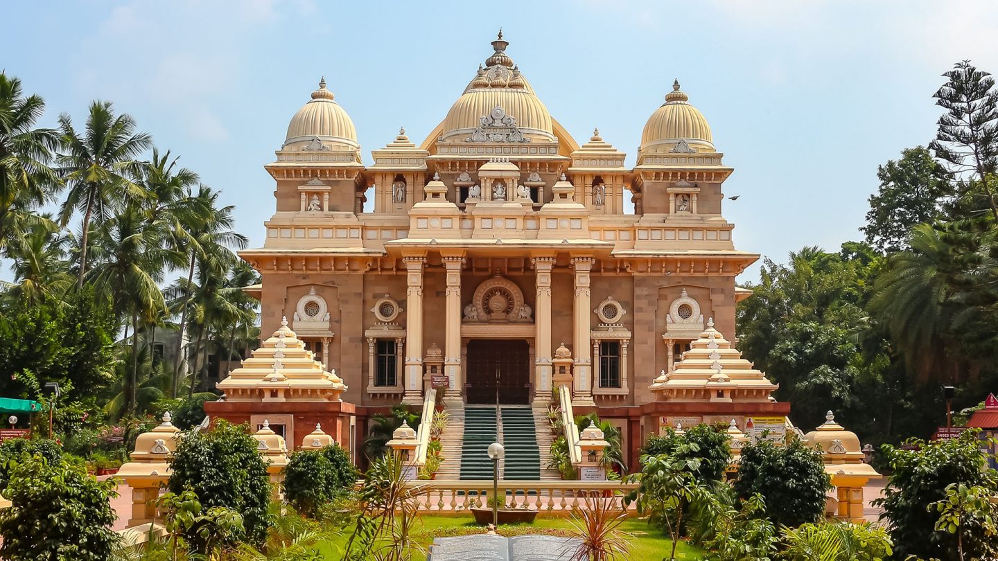 Hindu temple with ornate architecture, domes, and lush greenery under a clear blue sky.