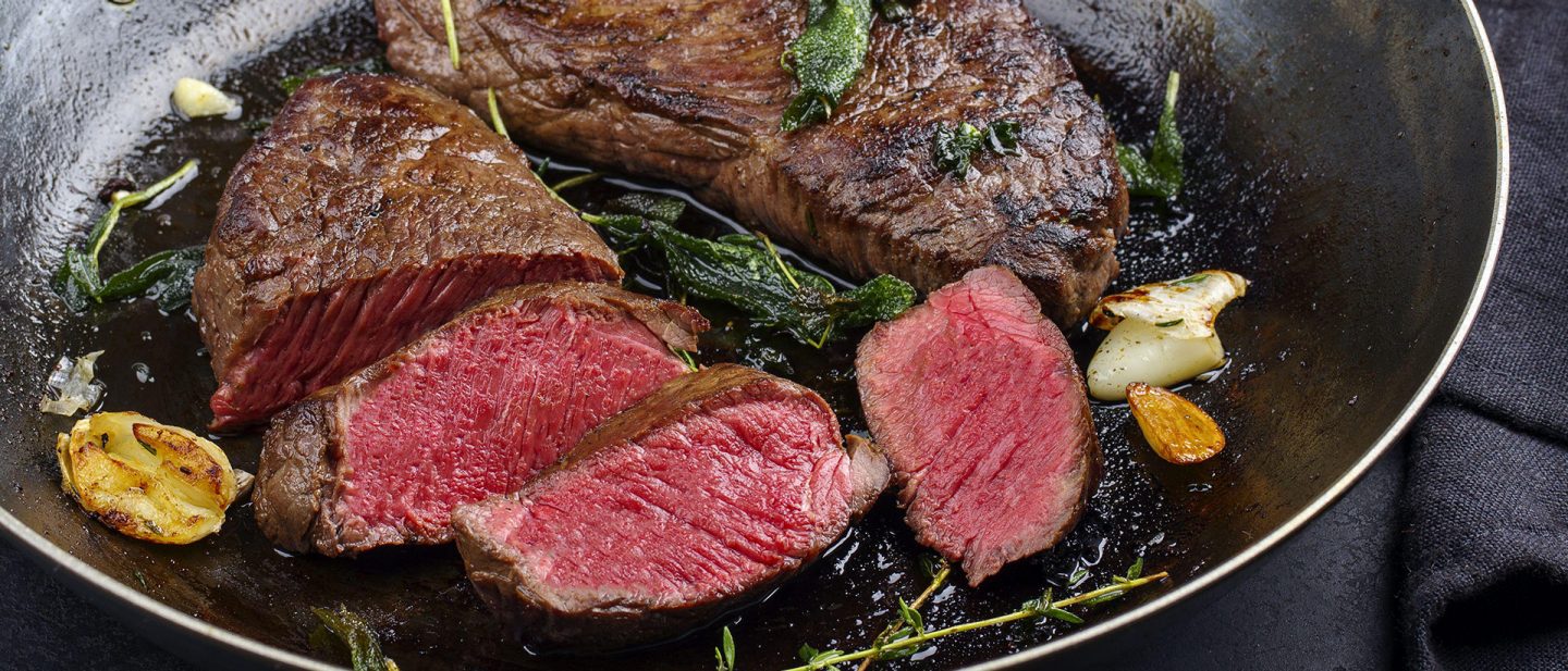 Juicy sliced steak with fresh herbs and garlic searing in a cast iron pan