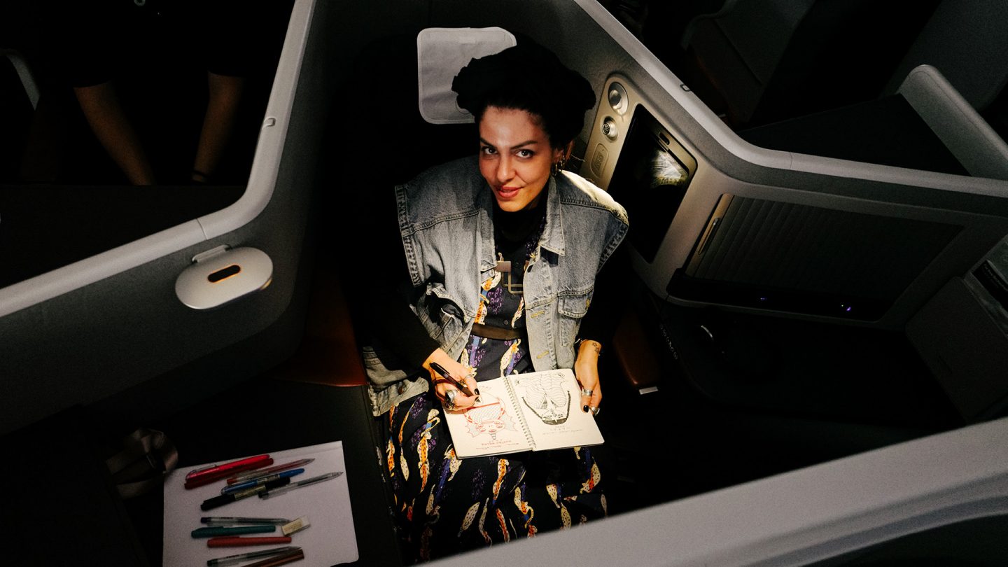 Une femme assise dans une cabine d'avion en train de dessiner dans un carnet de croquis