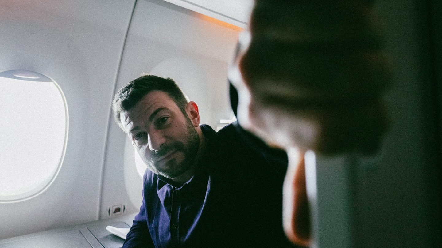 Ein Mann schaut auf eine andere Person im Flugzeug, die in der Nähe eines Fensters bei sanftem Tageslicht sitzt.